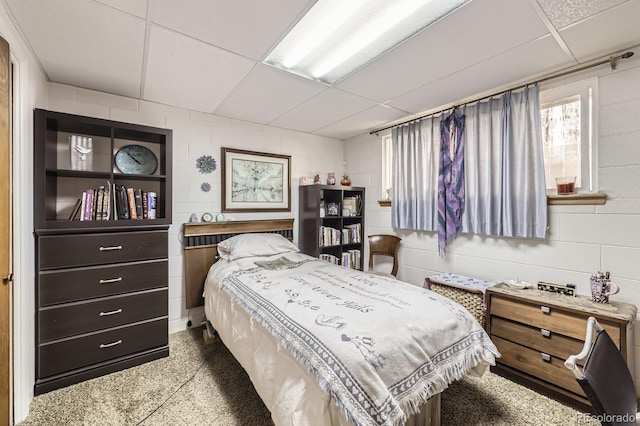 bedroom featuring a paneled ceiling, speckled floor, and concrete block wall