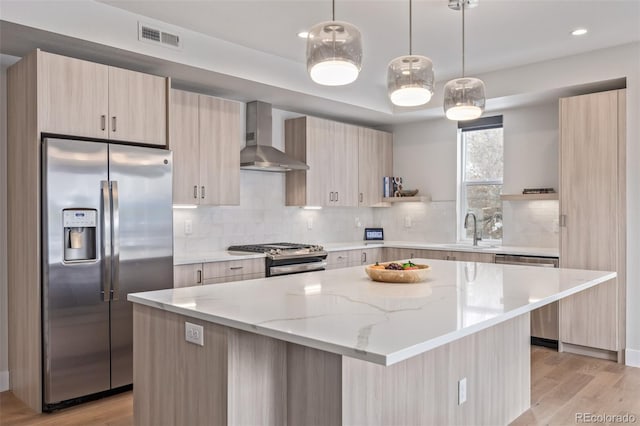 kitchen featuring appliances with stainless steel finishes, a center island, wall chimney range hood, and light brown cabinetry