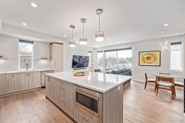 kitchen with sink, a center island, appliances with stainless steel finishes, pendant lighting, and light hardwood / wood-style floors