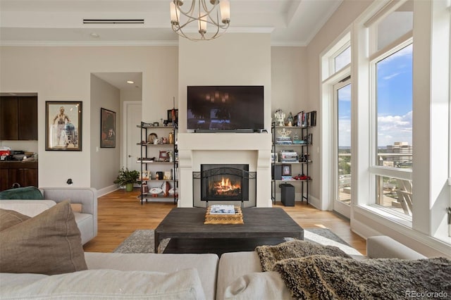 living room with ornamental molding, an inviting chandelier, and light wood-type flooring