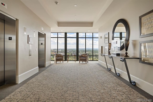 corridor featuring a wall of windows, elevator, dark carpet, and a raised ceiling