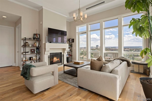 living area featuring a chandelier, light wood-style flooring, crown molding, and a lit fireplace