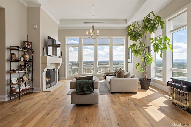 living room featuring a healthy amount of sunlight, ornamental molding, light hardwood / wood-style flooring, and an inviting chandelier