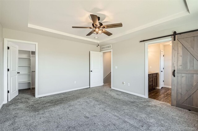 7263 Horsechestnut St, Wellington, CO 80549 - unfurnished bedroom featuring a barn door, a raised ceiling, dark colored carpet, baseboards, and a walk in closet