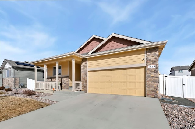 craftsman-style home featuring driveway, stone siding, an attached garage, covered porch, and a gate