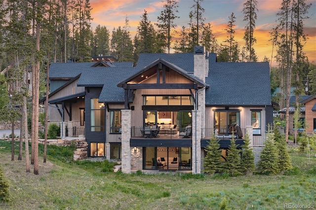 60 Barton Ridge Dr, Breckenridge, CO 80424 - back of property at dusk featuring stone siding, a chimney, roof with shingles, a lawn, and a patio area