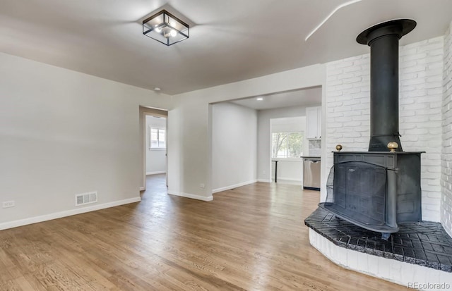 unfurnished living room featuring a healthy amount of sunlight, light wood-type flooring, and a wood stove