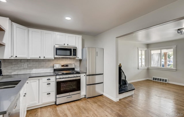 kitchen with appliances with stainless steel finishes, light wood-type flooring, tasteful backsplash, and white cabinetry