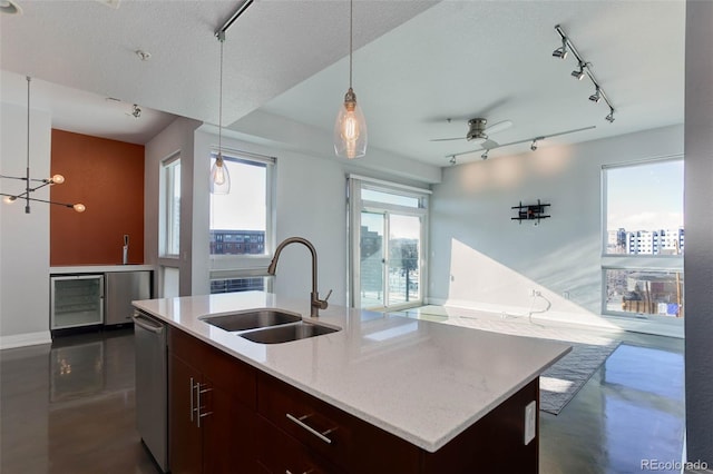 kitchen featuring a textured ceiling, ceiling fan, sink, decorative light fixtures, and a center island with sink