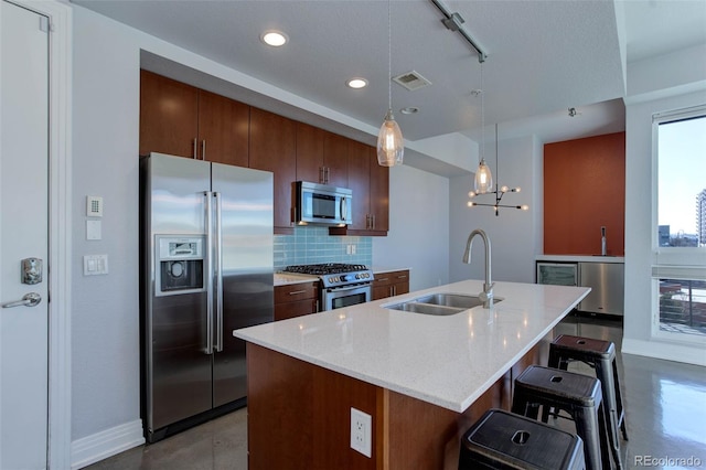 kitchen with decorative backsplash, appliances with stainless steel finishes, sink, a center island with sink, and hanging light fixtures