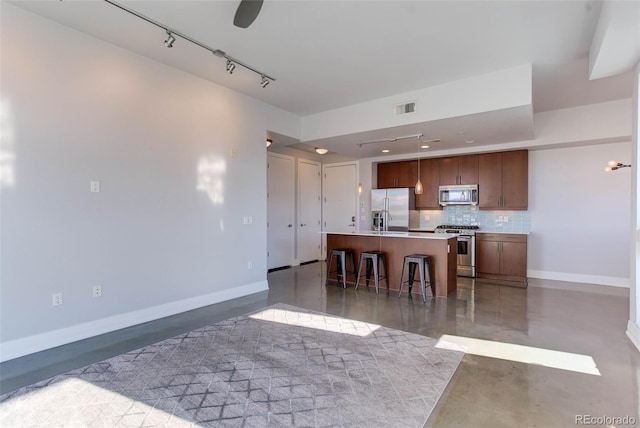 kitchen featuring a kitchen bar, backsplash, stainless steel appliances, a center island with sink, and concrete floors