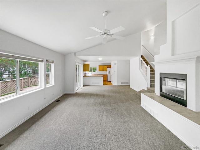 unfurnished living room featuring light carpet, stairs, a ceiling fan, a glass covered fireplace, and baseboards