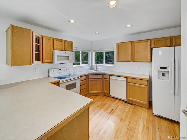 kitchen featuring white appliances, a sink, light wood-type flooring, light countertops, and glass insert cabinets