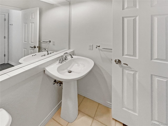 half bath with a sink, tile patterned floors, and baseboards