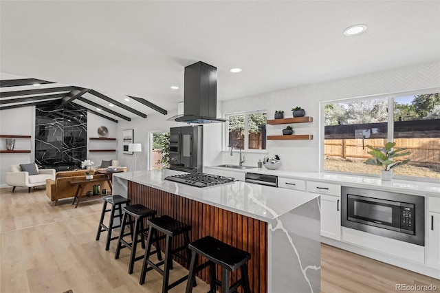 kitchen featuring built in microwave, stainless steel gas cooktop, a center island, island exhaust hood, and white cabinets