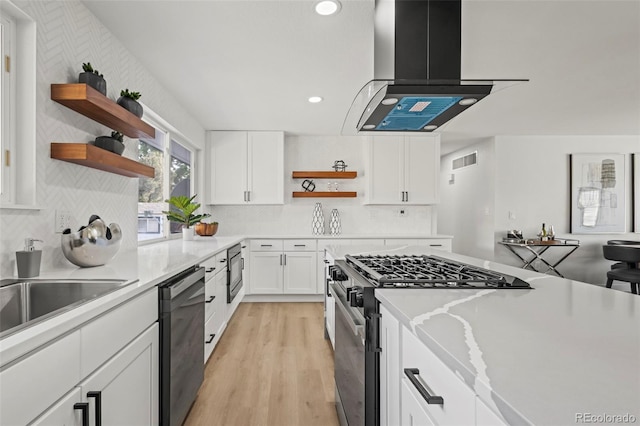 kitchen featuring appliances with stainless steel finishes, island range hood, white cabinetry, decorative backsplash, and light hardwood / wood-style flooring