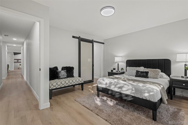 bedroom with a barn door and light wood-type flooring