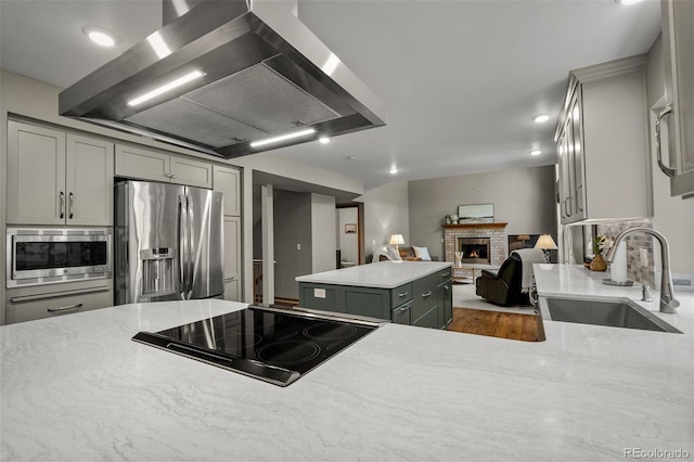 6285 Moccasin Pass Ct, Colorado Springs, CO 80919 - kitchen featuring appliances with stainless steel finishes, wall chimney range hood, gray cabinetry, a fireplace, and recessed lighting