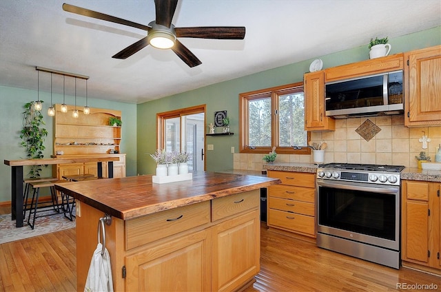 kitchen with wood counters, hanging light fixtures, light wood-type flooring, appliances with stainless steel finishes, and decorative backsplash