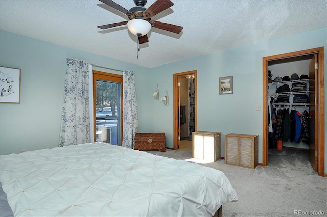 carpeted bedroom featuring ceiling fan, a walk in closet, a closet, and a textured ceiling