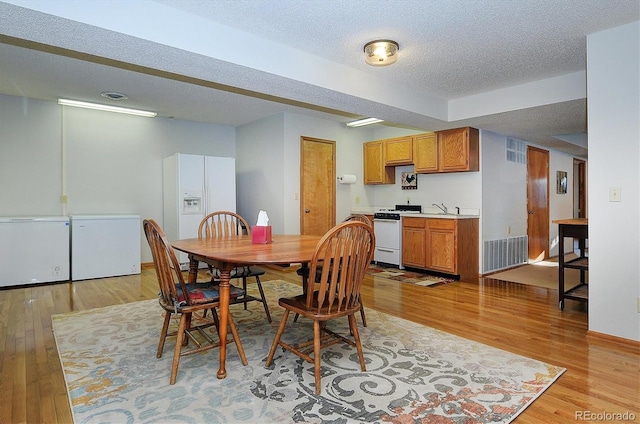 dining room featuring sink, a textured ceiling, and light wood-type flooring