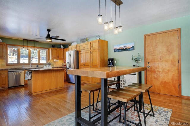 18360 Trail W Dr, Buena Vista, CO 81211 - kitchen with stainless steel appliances, light wood finished floors, a center island, ceiling fan, and decorative light fixtures