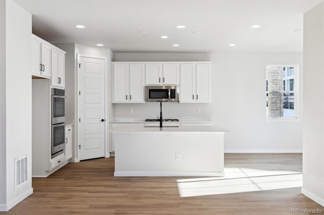 kitchen featuring white cabinetry, stainless steel appliances, light hardwood / wood-style floors, and a center island with sink