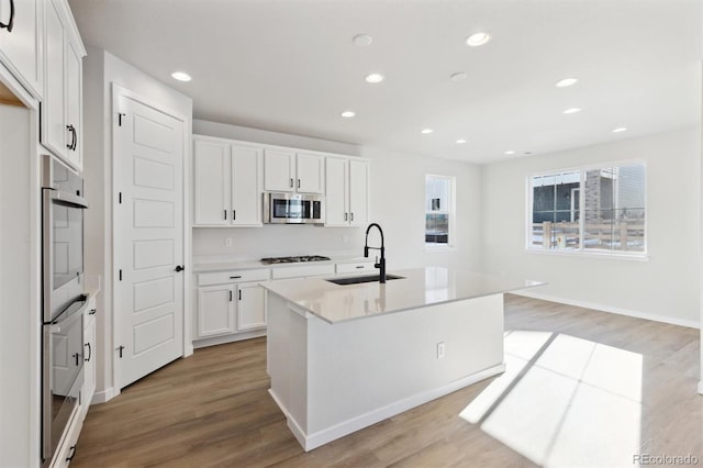 kitchen featuring white cabinets, sink, a kitchen island with sink, and light wood-type flooring