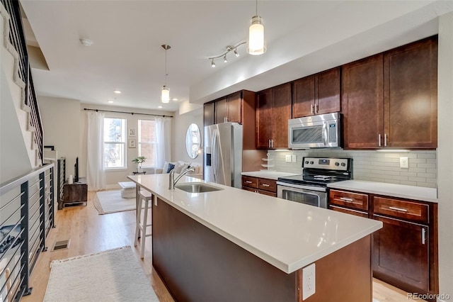 kitchen featuring stainless steel appliances, a sink, light wood-style floors, light countertops, and tasteful backsplash