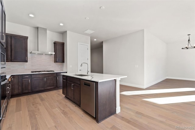 kitchen with pendant lighting, dishwasher, wall chimney exhaust hood, an island with sink, and gas cooktop