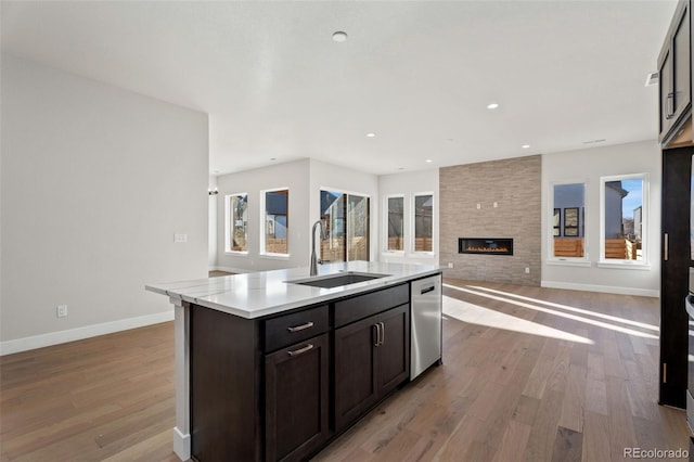 kitchen with dishwasher, an island with sink, sink, light wood-type flooring, and a tiled fireplace