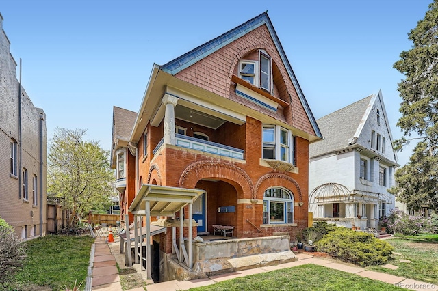 view of front facade featuring brick siding, fence, a shingled roof, and a balcony
