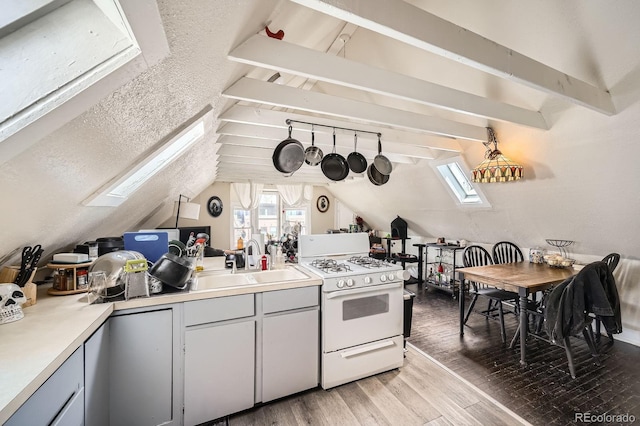 kitchen featuring white gas range, vaulted ceiling with skylight, light countertops, a sink, and light wood-style floors
