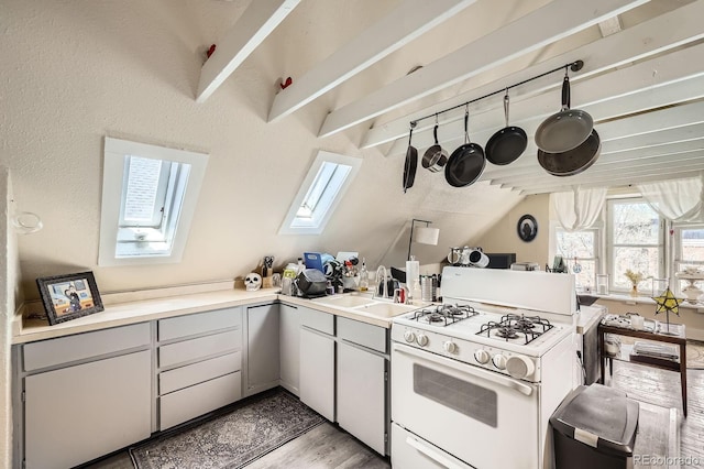 kitchen with a peninsula, gas range gas stove, light wood-type flooring, light countertops, and a sink