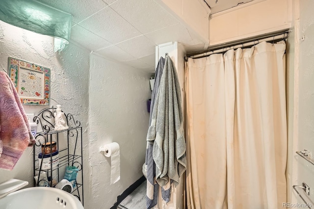 full bathroom with a textured wall and a drop ceiling