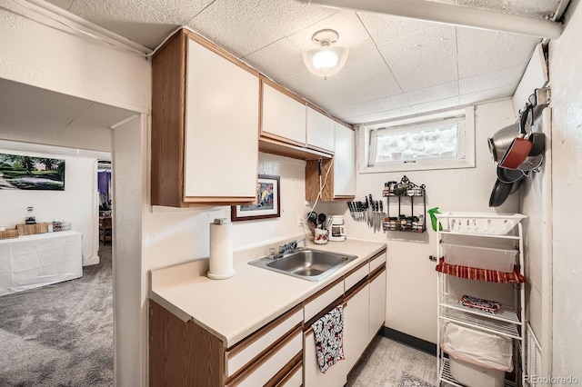 kitchen featuring light countertops, white cabinetry, a paneled ceiling, and a sink