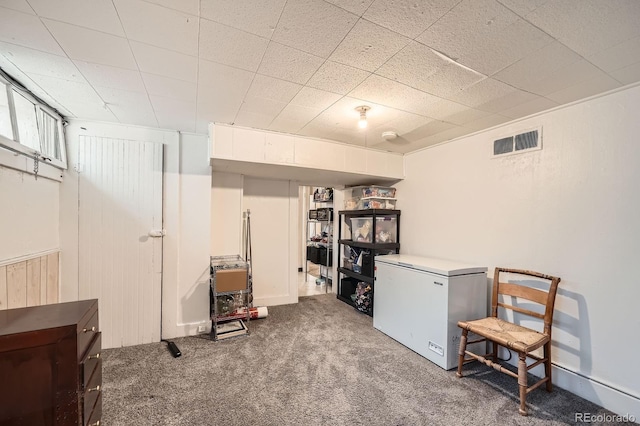 finished below grade area featuring carpet floors, visible vents, and white fridge
