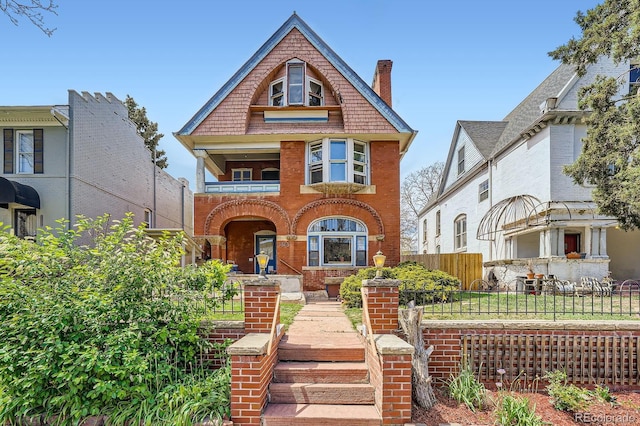 victorian-style house with brick siding, fence, and a balcony
