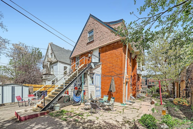 rear view of house featuring brick siding, stairs, a fenced backyard, and a storage unit