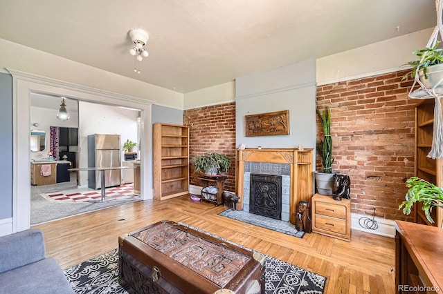 living room featuring a tiled fireplace, brick wall, and wood finished floors