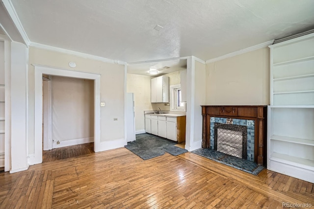 unfurnished living room featuring wood-type flooring, ornamental molding, a fireplace, baseboards, and a sink