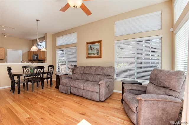 living room with a ceiling fan, baseboards, and light wood-style flooring