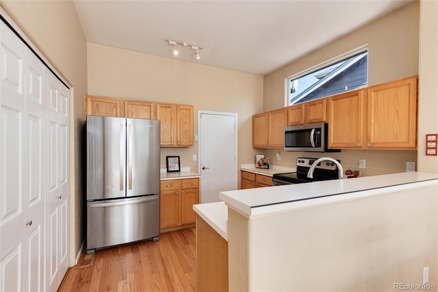 kitchen with a peninsula, light brown cabinets, light wood-type flooring, light countertops, and appliances with stainless steel finishes