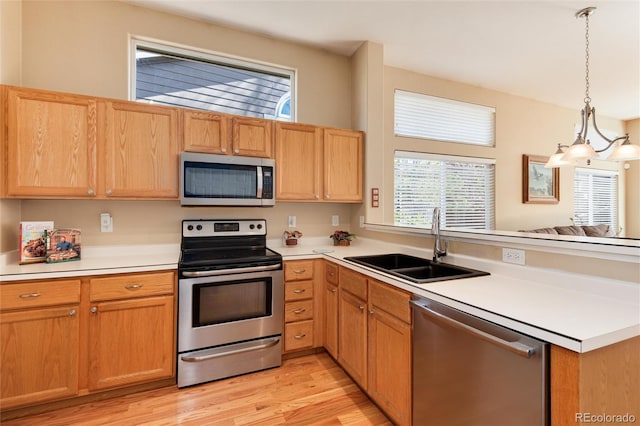 kitchen featuring a peninsula, light countertops, a sink, light wood finished floors, and stainless steel appliances