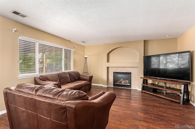 living room featuring a tile fireplace, dark hardwood / wood-style flooring, and a textured ceiling