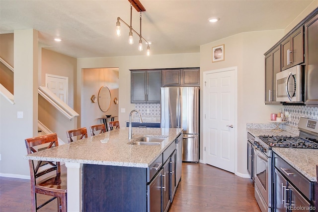 kitchen with decorative light fixtures, a kitchen island with sink, backsplash, appliances with stainless steel finishes, and sink