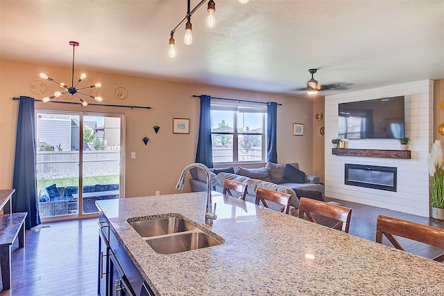 kitchen featuring a large fireplace, light stone countertops, hanging light fixtures, and sink