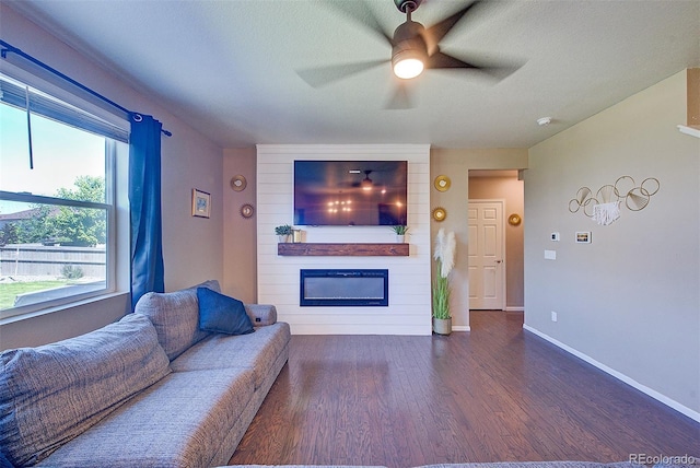 living room with a textured ceiling, a large fireplace, ceiling fan, and dark wood-type flooring