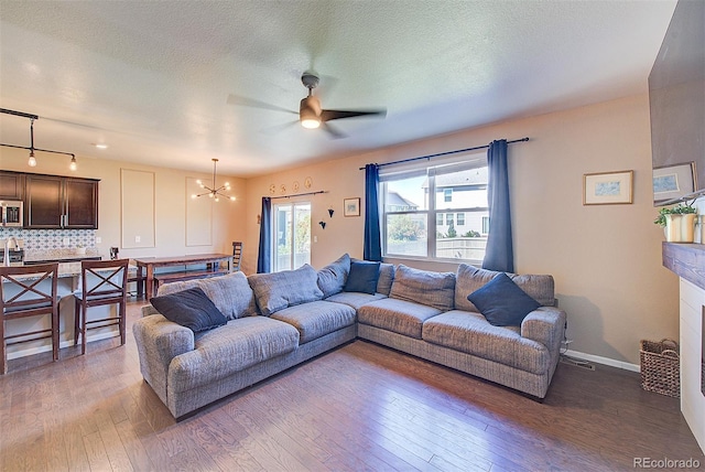 living room featuring a textured ceiling, ceiling fan with notable chandelier, and wood-type flooring