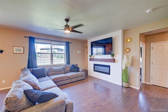 living room featuring dark hardwood / wood-style flooring, a textured ceiling, a large fireplace, and ceiling fan